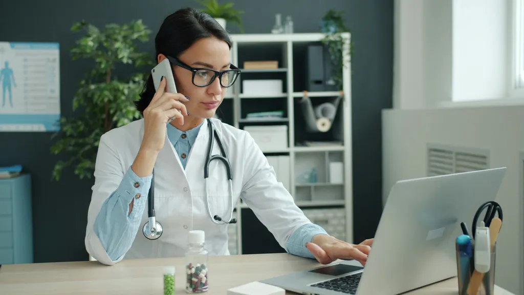 Doctor on phone, working on laptop in office